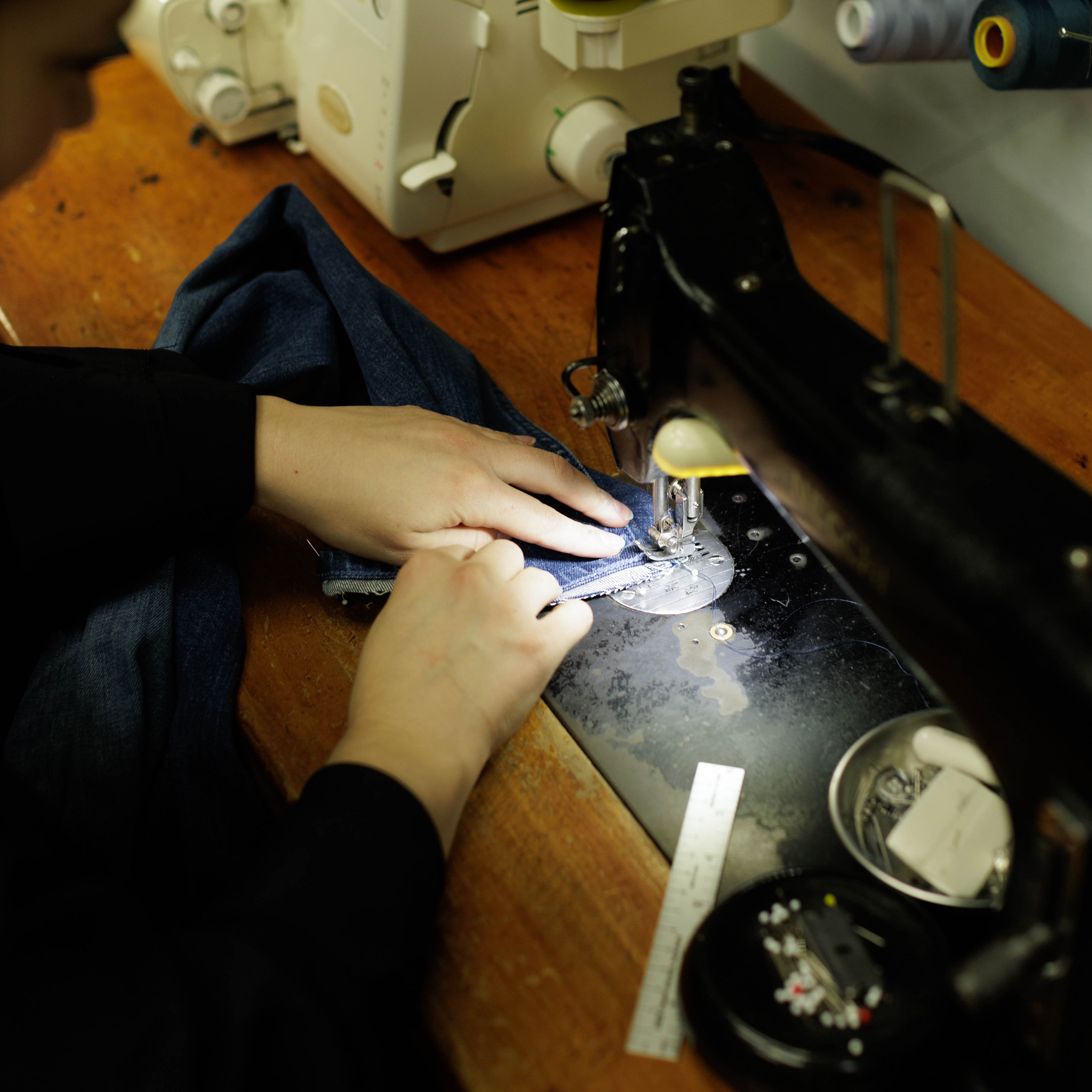 Person working on a sewing machine with various spools of thread in the background.