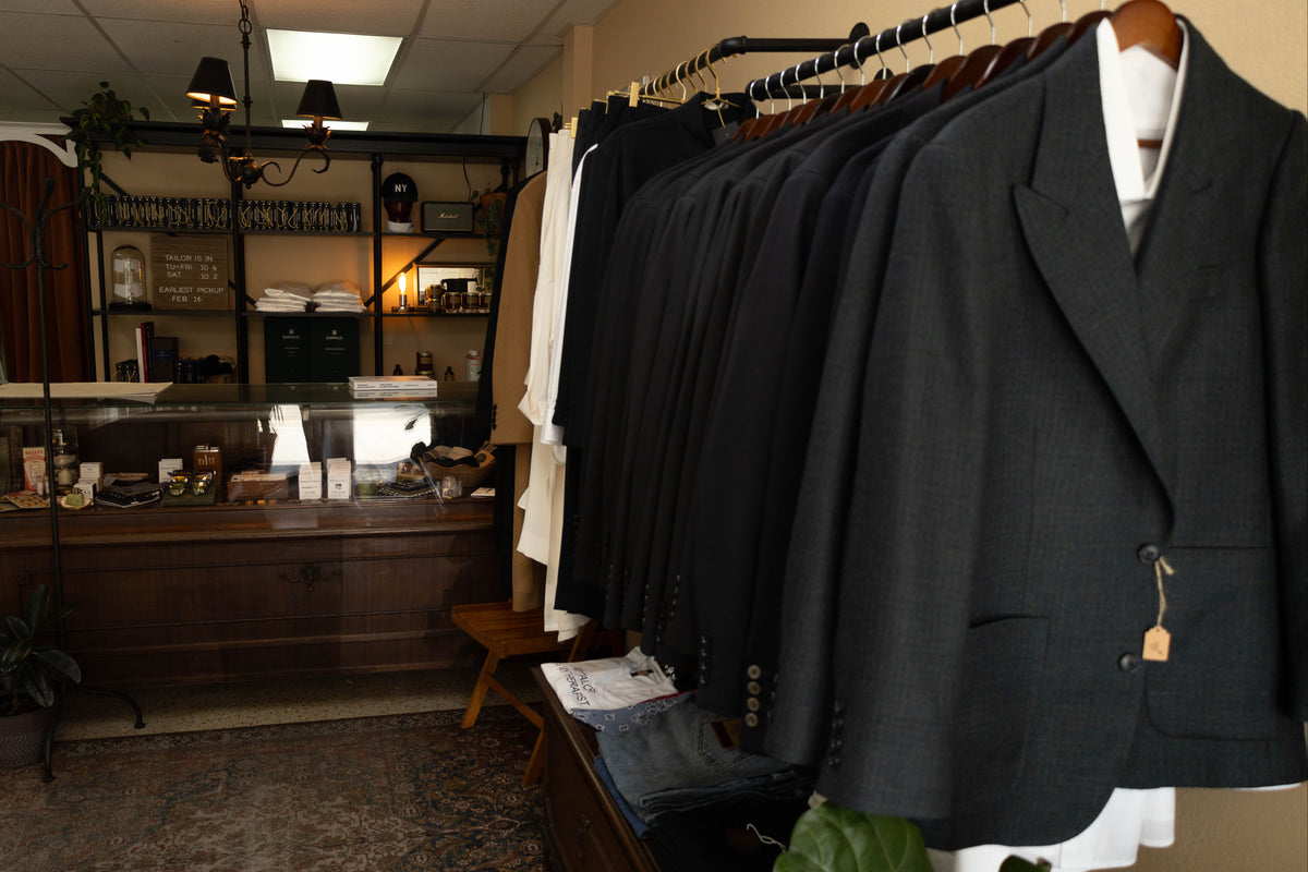 Clothing store interior with suits hanging on a rack and a counter in the background.